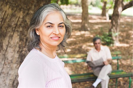 reading newspaper - Woman leaning against a tree with her husband reading a newspaper in the background, Lodi Gardens, New Delhi, India Stock Photo - Premium Royalty-Free, Code: 630-07071295