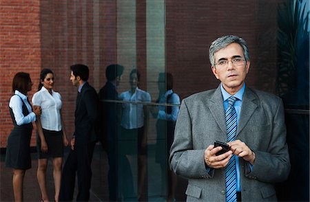 simsearch:630-07071521,k - Businessman using a mobile phone with their colleagues talking in the background Stock Photo - Premium Royalty-Free, Code: 630-07071588