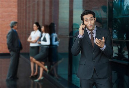 people shocked on phones - Businessman talking on a mobile phone with their colleagues in the background Stock Photo - Premium Royalty-Free, Code: 630-07071591