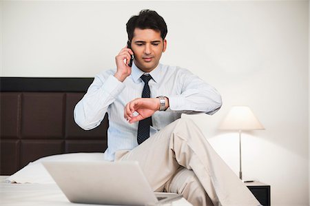 shirt on bed - Businessman talking on mobile phone and looking at his wristwatch Stock Photo - Premium Royalty-Free, Code: 630-07071621
