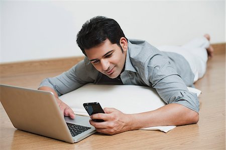 Man lying on a floor and working on a laptop and reading text message on a mobile phone Stock Photo - Premium Royalty-Free, Code: 630-07071692