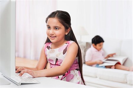 simsearch:630-07071840,k - Girl using a computer with her brother reading a book in the background Stock Photo - Premium Royalty-Free, Code: 630-07071748