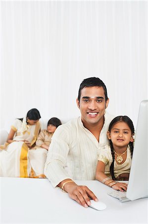 simsearch:630-07071840,k - South Indian man using a desktop computer with his daughter with other family in the background Stock Photo - Premium Royalty-Free, Code: 630-07071850