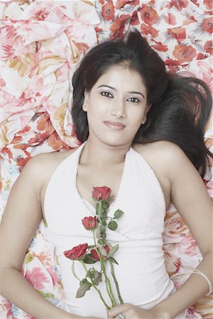 High angle view of a young woman lying on the bed holding roses Stock Photo - Premium Royalty-Free, Code: 630-01078124