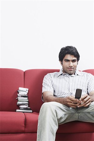 Close-up of a young man sitting on a couch operating a mobile phone Stock Photo - Premium Royalty-Free, Code: 630-01078796