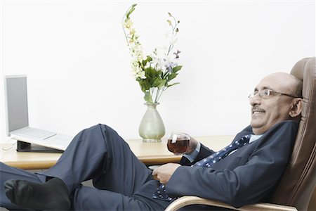 Side profile of a businessman reclining on a chair and holding a cup of black tea Stock Photo - Premium Royalty-Free, Code: 630-01079416