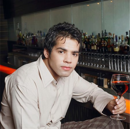 Portrait of a young man sitting at a bar counter and holding a glass of red wine Stock Photo - Premium Royalty-Free, Code: 630-01126893