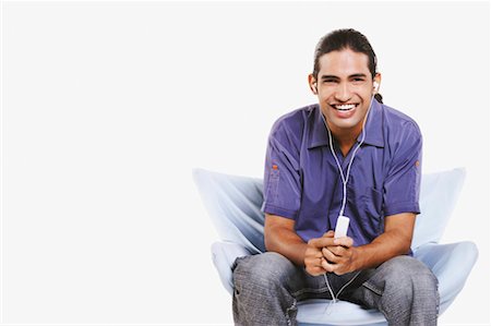 simsearch:630-01128257,k - Portrait of a young man sitting on a chair and listening to an MP3 player Stock Photo - Premium Royalty-Free, Code: 630-01128182