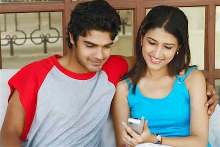 Close-up of a young couple sitting together holding a mobile phone Stock Photo - Premium Royalty-Free, Code: 630-01128196