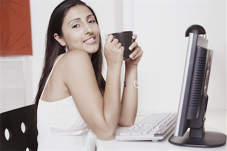 simsearch:630-01128103,k - Portrait of a young woman sitting in front of a computer and holding a mug Stock Photo - Premium Royalty-Free, Code: 630-01128557