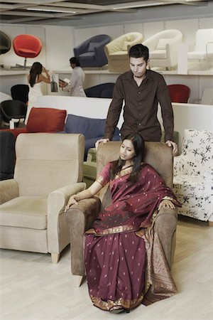 High angle view of a young woman sitting in an armchair in a furniture store with a young man standing behind her Stock Photo - Premium Royalty-Free, Code: 630-01130762