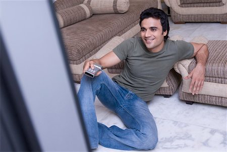 single man on the couch watching tv - Young man holding a remote control and smiling Stock Photo - Premium Royalty-Free, Code: 630-01192004