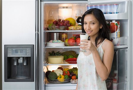 Portrait of a young woman standing near a refrigerator and holding a glass of milk Stock Photo - Premium Royalty-Free, Code: 630-01192010