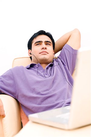 Young man sitting on a couch in front of a laptop and listening to music Stock Photo - Premium Royalty-Free, Code: 630-01192544