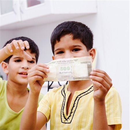 Portrait of a boy holding an Indian five hundred rupee note with his brother taking it Stock Photo - Premium Royalty-Free, Code: 630-01192625