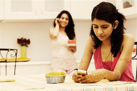 simsearch:630-01079908,k - Young woman listening to an MP3 player with a mid adult woman talking on a mobile phone in the background Stock Photo - Premium Royalty-Free, Code: 630-01192839