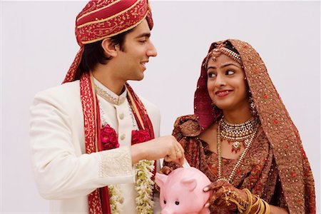 Bride holding a piggy bank with a groom putting money in it Stock Photo - Premium Royalty-Free, Code: 630-01192939