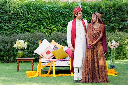 Newlywed couple in traditional wedding dress standing in front of a bed in a lawn Stock Photo - Premium Royalty-Free, Code: 630-01192988