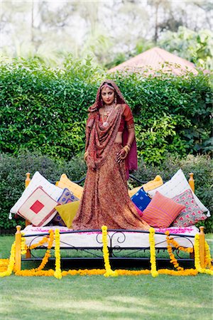 Portrait of a bride in a traditional wedding dress standing on the bed in a lawn Stock Photo - Premium Royalty-Free, Code: 630-01192991