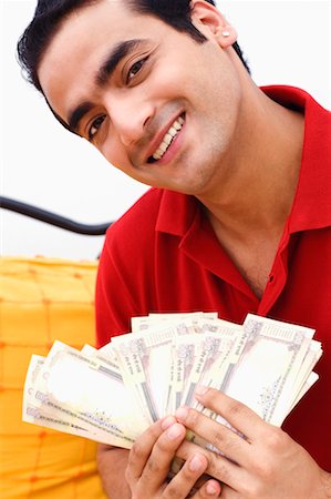 Close-up of a young man holding paper currency and smiling Stock Photo - Premium Royalty-Free, Code: 630-01296760