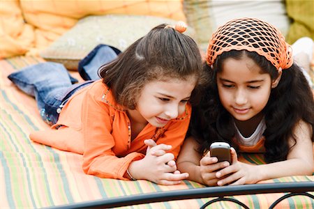 Girl with her sister looking at a mobile phone on the bed Stock Photo - Premium Royalty-Free, Code: 630-01296861