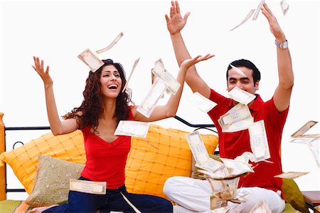 Young couple sitting on the bed and bank notes falling on them Stock Photo - Premium Royalty-Free, Code: 630-01297002