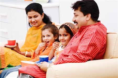 Two girls with their parents sitting on a couch and smiling Stock Photo - Premium Royalty-Free, Code: 630-01297135