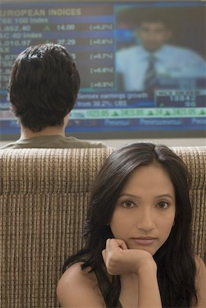 Rear view of a young man watching television with a young woman sitting behind him Stock Photo - Premium Royalty-Free, Code: 630-01490472