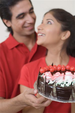 fruit birthday cake photo - Close-up of a young couple holding a chocolate cake and looking at each other Stock Photo - Premium Royalty-Free, Code: 630-01490841