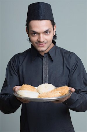 portraits one person muslim - Portrait of a young man holding a plate of sweets and smiling Stock Photo - Premium Royalty-Free, Code: 630-01490948