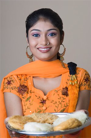 Portrait of a young woman holding a plate of sweets and smiling Stock Photo - Premium Royalty-Free, Code: 630-01490959