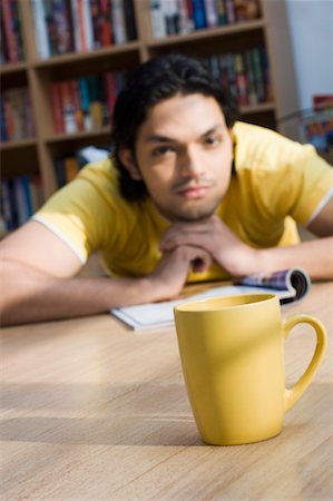 Close-up of a cup with a young man lying on the floor of a library in the background Stock Photo - Premium Royalty-Free, Code: 630-01490983