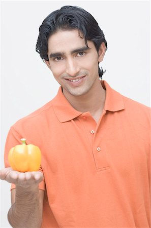 simsearch:630-01491487,k - Portrait of a young man holding a yellow bell pepper and smiling Fotografie stock - Premium Royalty-Free, Codice: 630-01491462