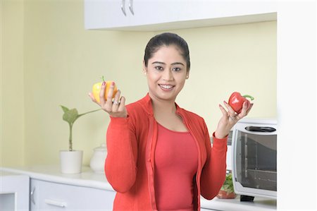 simsearch:630-01491487,k - Portrait of a young woman holding bell peppers and smiling Fotografie stock - Premium Royalty-Free, Codice: 630-01491486