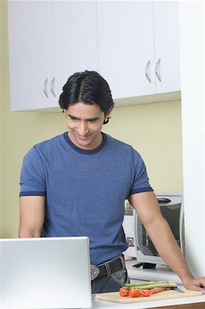 simsearch:630-01491487,k - Young man standing in a kitchen and using a laptop Fotografie stock - Premium Royalty-Free, Codice: 630-01491521