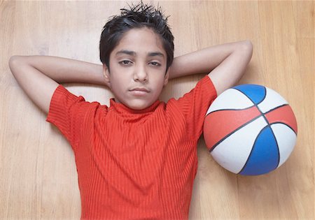Portrait of a boy lying on a hardwood floor with a basketball beside him Stock Photo - Premium Royalty-Free, Code: 630-01491549
