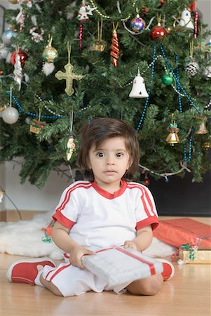 Portrait d'un garçon assis en face d'un arbre de Noël et tenant un cadeau de Noël Photographie de stock - Premium Libres de Droits, Code: 630-01491905