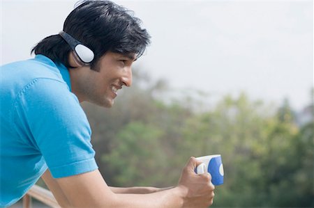 Side profile of a young man holding a cup of coffee and listening to music Stock Photo - Premium Royalty-Free, Code: 630-01492505