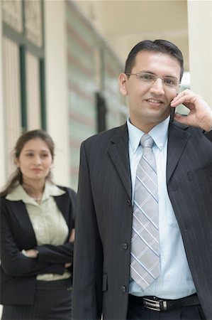 pakistani ethnicity (male) - Portrait of a businessman talking on a mobile phone with a businesswoman standing behind him Foto de stock - Sin royalties Premium, Código: 630-01492673