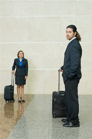 simsearch:693-06379884,k - Side profile of a businessman holding his luggage with a businesswoman standing in the background Stock Photo - Premium Royalty-Free, Code: 630-01492865