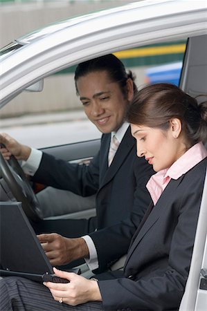 Side profile of a businesswoman using a laptop in a car with a businessman sitting beside her and smiling, Singapore Stock Photo - Premium Royalty-Free, Code: 630-01707756