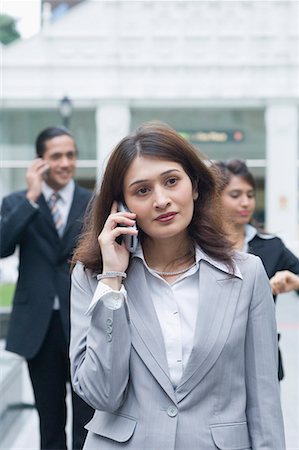simsearch:630-01079908,k - Businesswoman talking on a mobile phone with two business executives standing in the background Stock Photo - Premium Royalty-Free, Code: 630-01707786