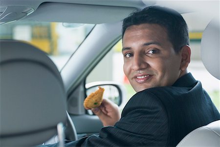 Portrait of a businessman smiling in a car and holding a gujiya Stock Photo - Premium Royalty-Free, Code: 630-01707820
