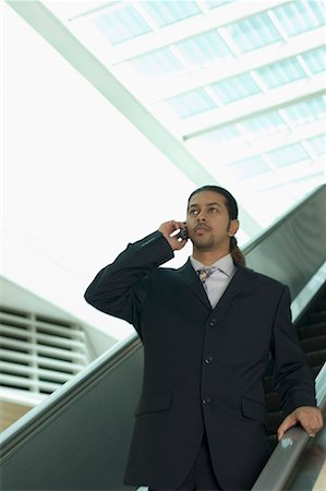 Low angle view of a businessman standing on an escalator and talking on a mobile phone Stock Photo - Premium Royalty-Free, Code: 630-01707907