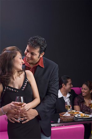 restaurant with young friends - Young men embracing a young woman with a young couple sitting on a couch in the background Stock Photo - Premium Royalty-Free, Code: 630-01707954