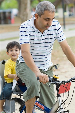 Mid adult man riding a bicycle with his son sitting behind him Foto de stock - Sin royalties Premium, Código: 630-01708016