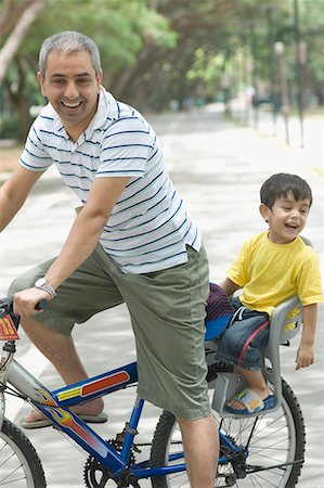 simsearch:630-01709612,k - Mid adult man riding a bicycle with his son sitting behind him Stock Photo - Premium Royalty-Free, Code: 630-01708025