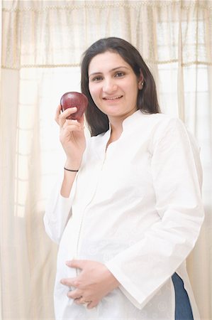 Portrait of a pregnant woman holding an apple and smiling Stock Photo - Premium Royalty-Free, Code: 630-01708228