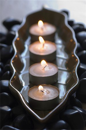 Close-up of four aromatherapy candles burning in a tray with black pebbles Fotografie stock - Premium Royalty-Free, Codice: 630-01708260