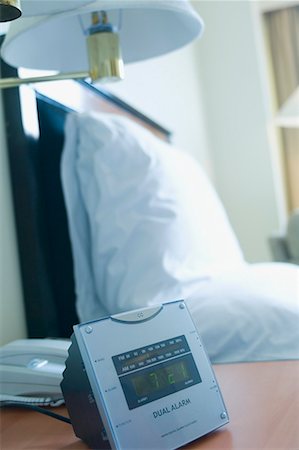 simsearch:630-01708436,k - Alarm clock and a lamp shade with a telephone on the night table beside a bed in a hotel room Fotografie stock - Premium Royalty-Free, Codice: 630-01708430